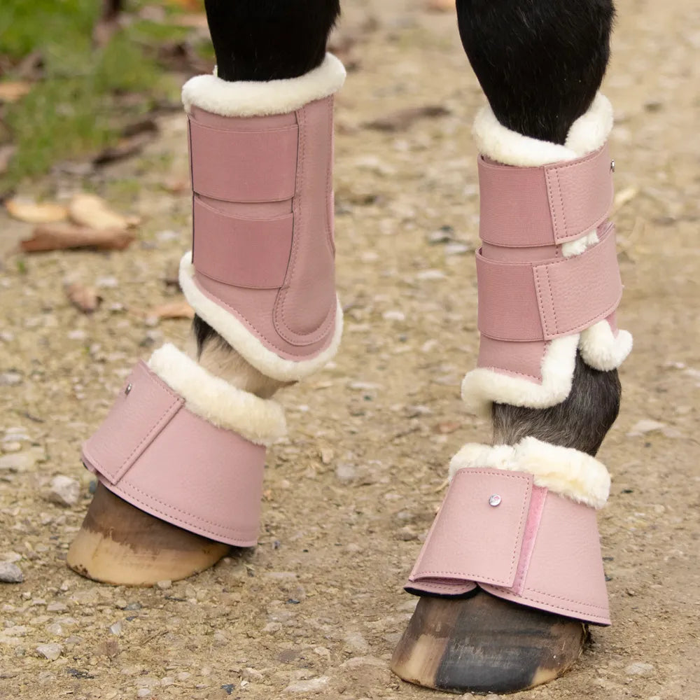 Pink protective leg wraps with white fur lining on horse legs on a gravel surface.