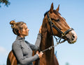 Woman leading a brown horse outdoors with a clear blue sky.