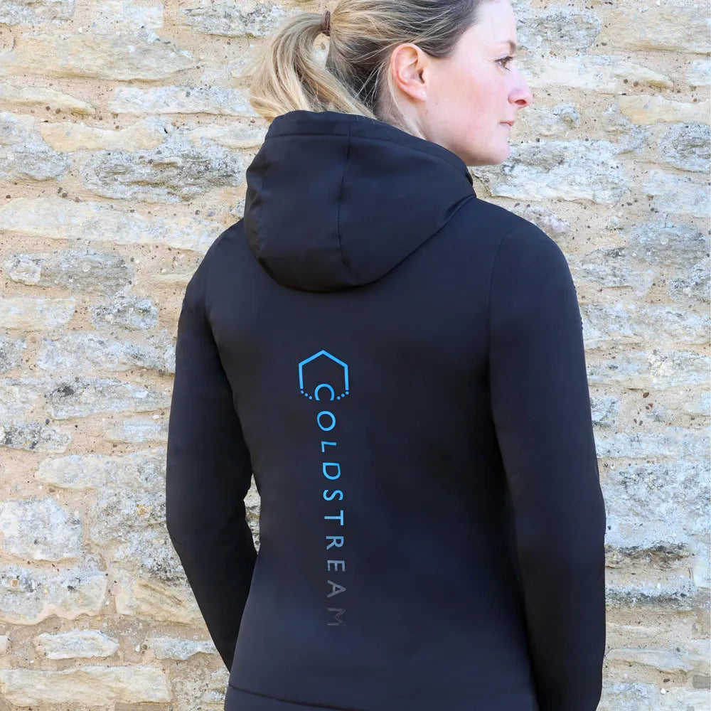 Person wearing a black hoodie with 'Coldstream' logo on the back against a stone wall.