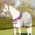 White horse wearing a purple and gray rug in an outdoor setting with trees and grass.